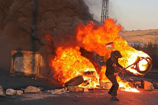17일(현지시간) 요르단강 서안 도시 라말라 인근 베이트 엘 정착촌에서 한 팔레스타인 주민이 타이어를 불태우며 최근 이스라엘과 팔레스타인 사이에서 벌어지고 있는 무력 충돌 사태를 규탄하고 있다. AFP연합뉴스