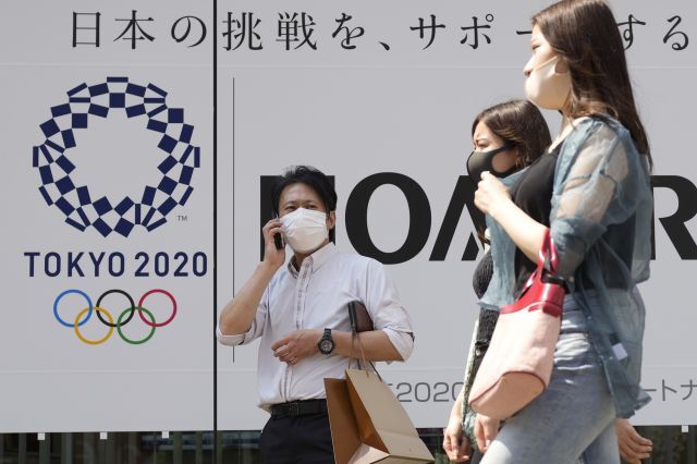 일본 수도 도쿄에서 25일 코로나19 예방 마스크를 쓴 시민들이 개막이 채 한 달도 남지 않은 도쿄올림픽의 포스터 앞을 지나고 있다. 일본은 최근 코로나19 신규 확진자 수가 연일 1700명대를 기록해 올림픽을 코앞에 두고 재차 증가 조짐을 보이고 있다. 연합뉴스