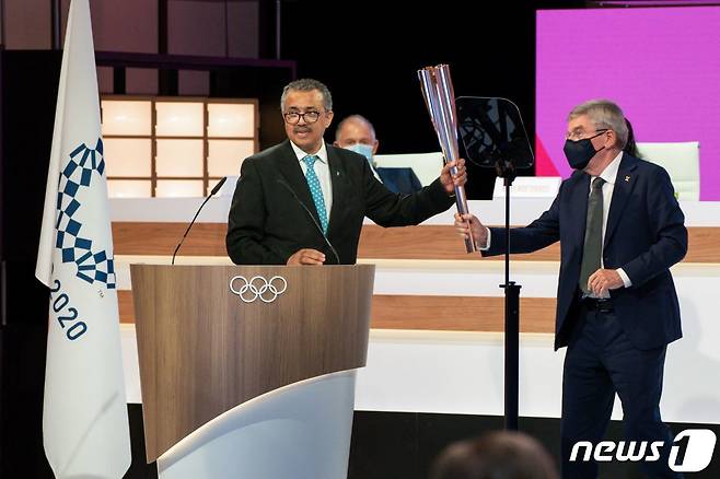 테워드로스 아드하놈 거브러여수스 WHO 사무총장이 지난 21일 도쿄에서 열린 IOC 총회에서 토마스 바흐 IOC 위원장에게 올림픽 성화를 건네받고 있다. © AFP=뉴스1