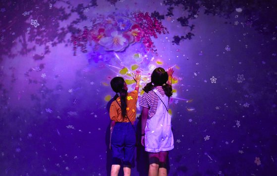흩날리는 꽃잎’의 벽에 손을 대면 나뭇가지·새싹과 함께 아름다운 꽃이 핀다. 벽을 장식한 꽃을 바라보고 있는 두 사람.