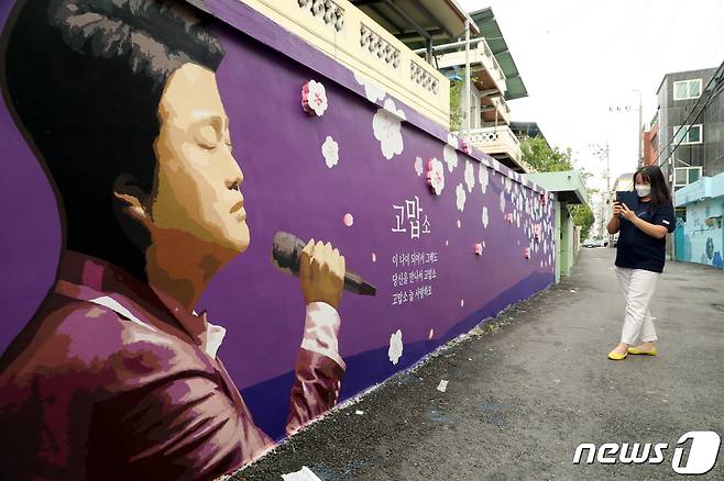 경북 김천예고 옆 교동연화지로 가는 골목길에 조성된 '트바로티 김호중 소리길'에서 팬카페 '아리스' 한 회원이 담장 벽화에 그려진 김호중의 그림을 카메라에 담고 있다. 2021.9.20/뉴스1 © News1 정우용 기자
