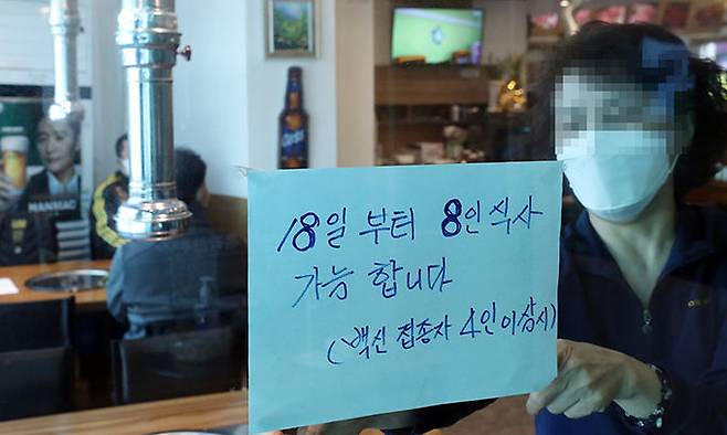 “8명까지 받습니다” 안내문 17일 서울 종로구의 한 식당 직원이 18일부터 백신 접종 완료자 4인 이상 시 8인까지 식사가 가능하다는 안내문을 붙이고 있다. 위드 코로나에 한발 가까워지면서 기대감이 커지고 있다. 뉴스1