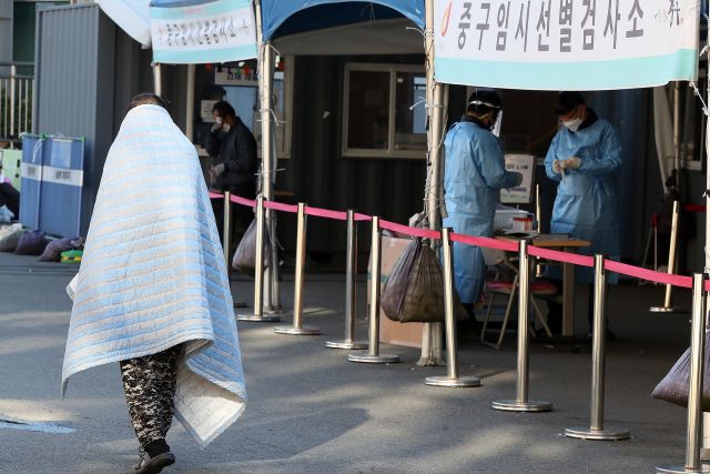 전국 대부분 지역에 한파특보가 내려진 지난 17일 오전 서울 중구 서울역광장 임시선별검사소에서 한 시민이 담요를 덮고 있다. 뉴시스