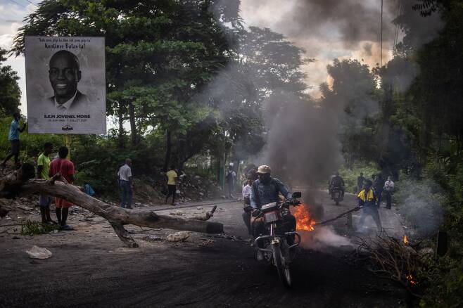 지난 21일(현지 시각) 중미 카리브해 섬나라 아이티의 수도 포르토프랭스에서 가스 등 연료 부족에 항의하는 시위가 벌어진 가운데, 분노한 시민들이 도로 위에 나무로 바리케이드를 치고 한쪽에선 나뭇가지에 불을 지르고 있다. 바리케이드 옆에는 지난 7월 암살된 조브넬 모이즈 대통령의 사진이 걸려 있다. 아이티는 무장 갱단 90여 개가 전국의 40%를 지배하는 등 극도의 무정부 상태가 지속되고 있다. /로이터 연합뉴스