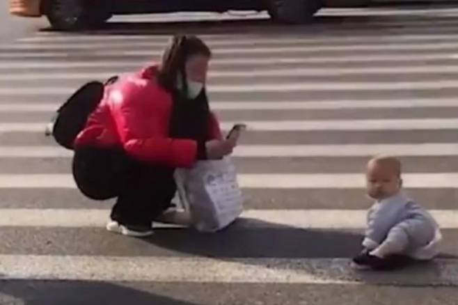 지난 25일 허베이성 스자좡시의 한 도로에서 촬영된 장면. 차가 지나다니는 횡단보도 위에 아기가 기어다니고 있고 엄마로 추정되는 여성은 그 모습을 핸드폰으로 촬영하고 있다. /사진=웨이보