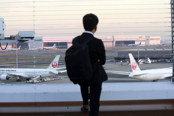 한 남자가 지난달 29일 도쿄 하네다 국제공항에 대기 중인 일본항공 비행기들을 보고 있다. NHK 방송은 1일 일본이 새로운 바이러스 변종을 막기 위해 한 달 동안 들어오는 모든 항공편의 신규 예약을 중단할 것이라고 밝혔다. AP 연합뉴스 2021-12-01