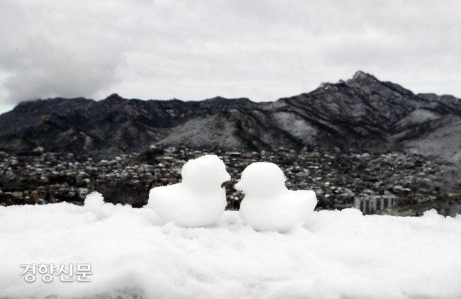 서울 북악산 팔각정 난간에 지난해 3월  흰 눈 덮인 북한산을 배경으로 눈오리 한 쌍이 놓여 있다. 강윤중 기자