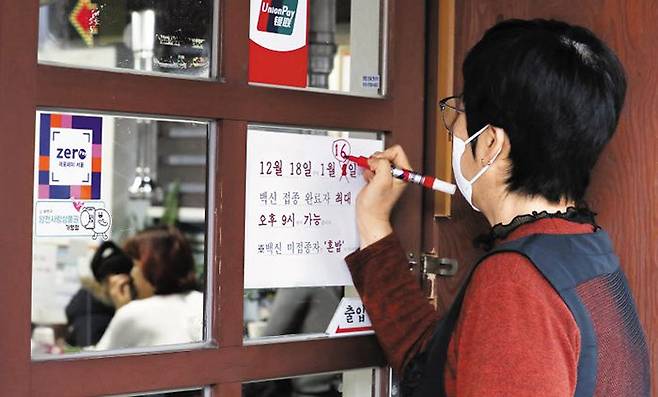 정부가 현행 사회적 거리 두기를 1월 16일까지 2주 연장하겠다는 방침을 밝힌 지난해 12월 31일 서울의 한 식당에서 안내 문구를 수정하고 있다. /뉴시스