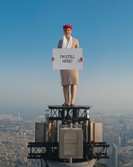 작년 8월에 이어, UAE 항공이 부르즈 칼리파 꼭대기에서 다시 제작한 광고 동영상에서 이 항공사 승무원인 니콜 스미스-루드비크가 "아직 여기 있다"는 메시지 보드를 들어 보이고 있다./UAE항공 스크린샷