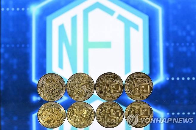 (AFP=연합뉴스) 지난달 30일 영국 런던에서 NFT라고 새겨진 스크린을 배경으로 촬영된 가상화폐 기념주화. 2022.1.26.