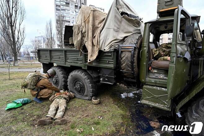 우크라이나 군 의무병이 25일(현지시간) 우크라이나 수도 키예프에서 공습대원들과 교전 중 총격을 당해 차량 옆에 누워 있는 우크라이나 군복을 입은 러시아 군인의 시신을 살펴보고 있다. © afp=뉴스1 © News1 포토공용 기자