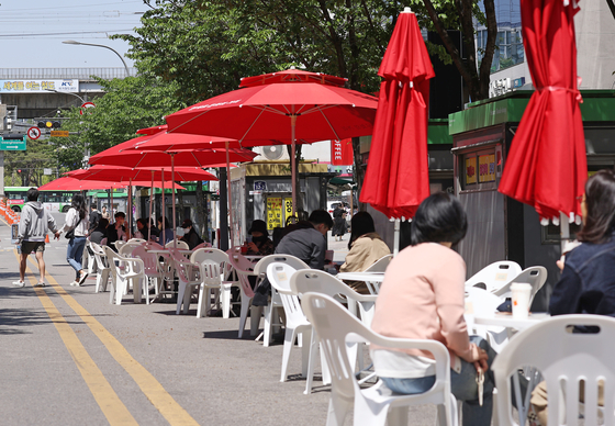 People chat under parasols installed at Sinchon's Yonsei-ro in Seodaemun District, western Seoul, on Sunday afternoon. The district announced that it will install parasols every Friday from 2 p.m. to 10 p.m. Sunday night on the Yonsei-ro car-free street to help revitalize the street. [YONHAP]