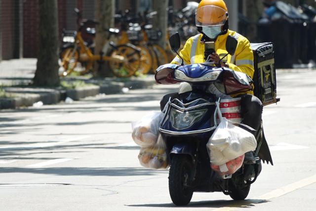 14일 코로나19 확산으로 48일째 봉쇄 중인 중국 상하이 창닝구의 도로에서 메이퇀 소속 배달기사가 식료품을 단 주머니를 매단 채 도로 위를 달려가고 있다. 상하이=연합뉴스