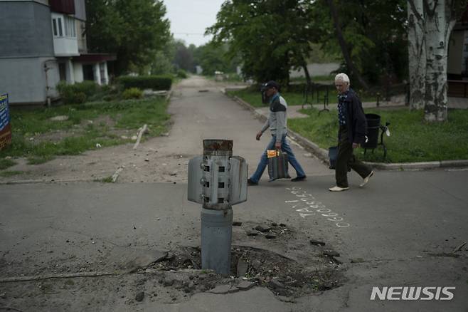 [리시찬스크=AP/뉴시스]지난달 13일(현지시간) 우크라이나 루한스크주 리시찬스크에서 주민들이 도로에 박힌 로켓 주변을 지나고 있다. 2022.05.14.