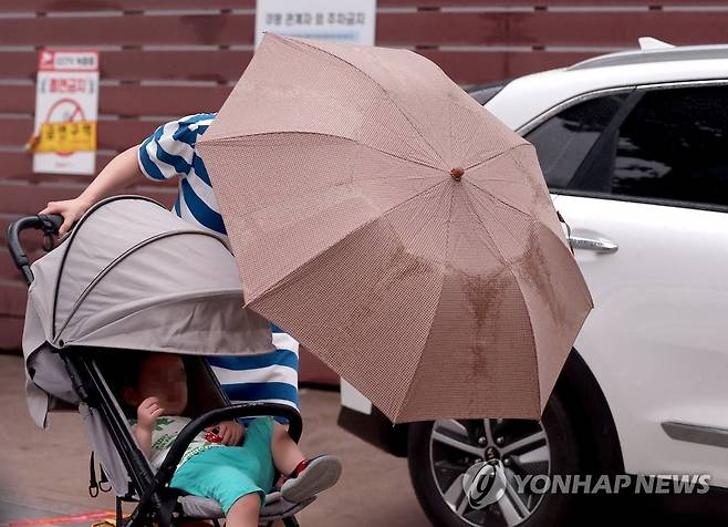 '비 맞으면 안돼' 장마가 계속되는 6월 29일 오후 서울 충정로를 지나던 한 시민이 비가 내리자 우산을 아이에게 씌워주고 있다. [연합뉴스 자료사진]