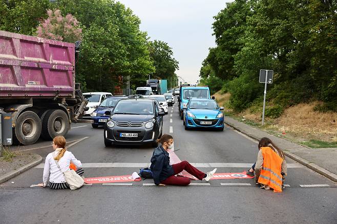 독일 환경단체 '마지막 세대'(Letzte Generation) 소속 운동가들이 30일(현지시간) 수도 베를린의 한 도로에서 '화석 연료 광기를 끝내자!'라는 표어가 적힌 팻말 깔고 앉아 차량 통행을 막고 있다. 2022.6.30/로이터 연합뉴스