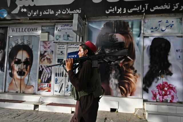 지난해 8월 이슬람 무장세력 탈레반에 장악된 아프가니스탄 수도 카불에서 어깨에 소총을 멘 한 탈레반 병사가 여성 모델들의 사진이 훼손된 미용실 앞을 지나고 있다. 카불=AFP 연합뉴스