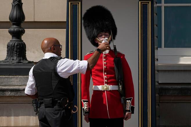 영국 런던의 버킹엄궁 밖에서 한 경찰관이 곰털 모자를 쓰고 근무하는 왕실 근위병에게 물을 주고 있다.