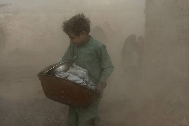 지난 8월 20일 9살 소년이 도구를 담은 통을 가지고 이동하다 먼지가 일자 고개를 돌리고 있다. 카불/AP 연합뉴스