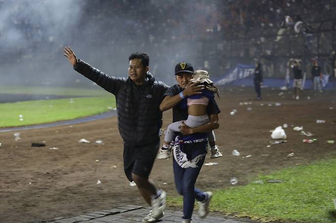 1일(현지시각) 인도네시아 동자바주 말랑시의 칸주루한 경기장에서 한 관중이 어린이를 대피시키고 있다. 이날 패배팀을 응원하는 관중이 경기장에 난입하고 경찰이 최루탄을 발사하면서 최소 125명이 숨지는 사고가 발생했다. 자바/EPA 연합뉴스