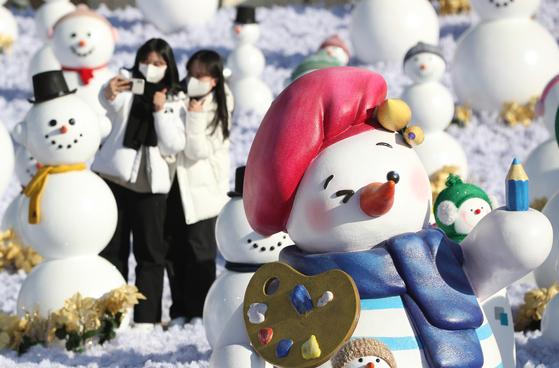 Visitors take pictures with snowman decorations set up at the ″Snowman World″ festival at the Everland theme park in Gyeonggi on Thursday. The snowman installations will be in place until March 1 next year. [NEWS1]