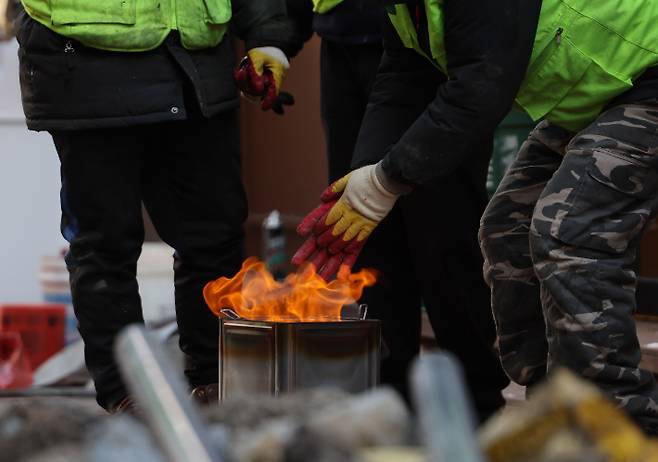 강추위가 이어진 지난달 16일 오전 서울 명동 거리의 한 공사 현장에서 관계자들이 고체연료로 몸을 녹여가며 작업하고 있다. 연합뉴스