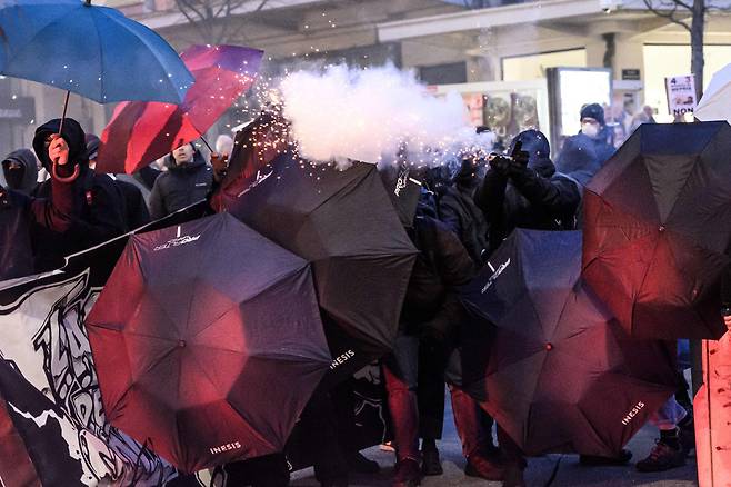 프랑스 전역에서 정부의 연금개혁에 반대하는 시위가 격화하는 가운데 21일(현지 시각) 서부 낭트에서 시민들이 우산 뒤에 숨은 채 경찰을 향해 폭죽을 쏘고 있다.