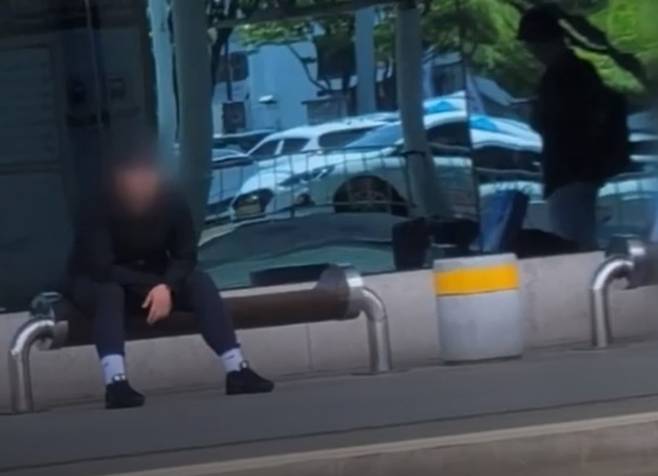 지난 26일 대구공항에 착륙 중이던 비행기 비상구 문을 강제로 연 혐의를 받는 A(33)씨가 오후 1시3분쯤 대구공항 청사 밖 버스정류장에 앉아있는 모습. MBC 방송화면 갈무리