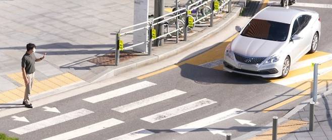 무신호 횡단보도에서 보행자가 손을 올려 길을 건너려는 의사를 표시하고 있다. 사진 도로교통공단