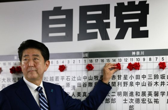 아베 신조 전 일본 총리가 지난 2017년 열린 중의원 선거에서 당선자의 이름 위에 꽃을 달고 있다. AP=연합뉴스