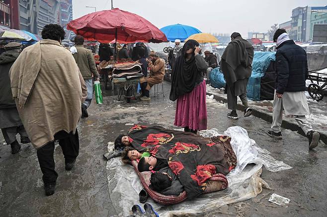 2022년 1월 19일 아프가니스탄 카불의 시장에서 한 여성이 잠을 자고 있는 아이들 옆에서 도움을 요청하고 있다. / AFP 연합뉴스