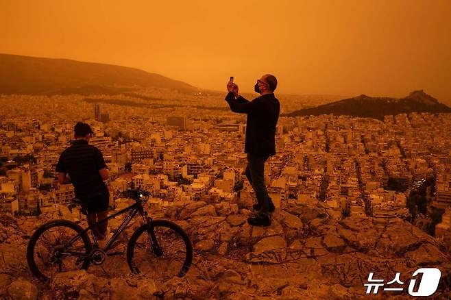 23일(현지시간) 남유럽 그리스 아테네 상공이 아프리카 사하라 사막에서 바람을 타고 넘어온 황색 모래로 뿌옇다. 한 남성이 아테네 투르코보니아 언덕에서 사진을 찍고 있다. 2024.04.23 ⓒ AFP=뉴스1 ⓒ News1 최종일 기자