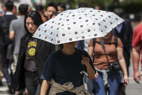 지난 26일 서울 종로구 광화문네거리에서 양산을 쓴 시민이 이동하고 있다. 뉴시스