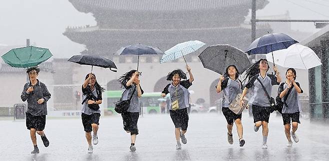 장대비 쏟아져도, 함께 있어 즐거운 우리들 - 2일 장맛비가 내리는 서울 광화문광장에서 우산 쓴 학생들이 함께 달리고 있다. 기상청은 때이른 폭염과 길어지는 장마 등을 감안해 사계절 가운데 ‘여름’ 기간을 6~8월에서 확대하는 방안을 추진한다. /뉴스1