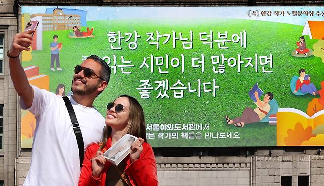 한강 작가의 책을 들고 있는 외국인 관광객이 서울도서관 외벽에 걸린 노벨문학상 수상 기념 걸개를 배경으로 셀카를 찍고 있습니다. 배경 글귀처럼 한강 작가의 수상을 계기로 책 읽는 시민들이 더 많아지길 바랍니다. 이충우 기자