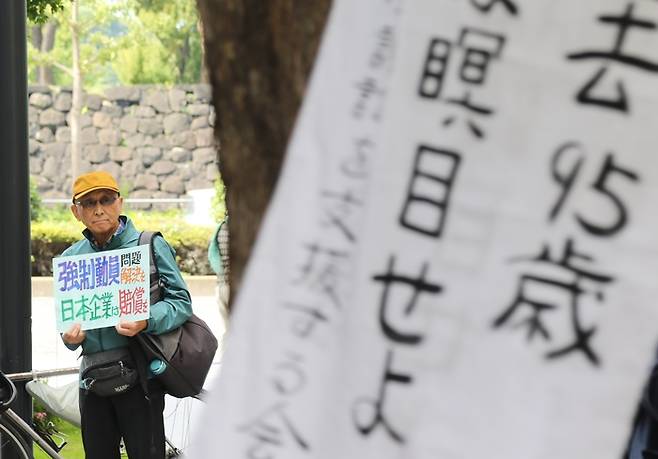 일본 도쿄 지요다구 미쓰비시상사 앞에서 지난달 11일 열린 제540회 금요행동에서 참가자가 ‘강제동원 문제 해결을, 일본기업은 배상을’이라고 적힌 팻말을 들고 서 있다. 일본 시민단체는 2007년부터 금요행동이라는 집회를 통해 징용 소송 피고 기업을 상대로 배상과 사죄를 요구하고 있다. 연합뉴스