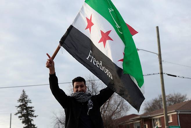 8일(현지시각) 미국 미시간주 디어본에서 시리아 반군이 시리아의 바샤르 알 아사드 대통령을 축출했다고 발표한 후 시리아계 미국인과 지지자들이 축하하는 가운데 한 사람이 '자유'라고 쓰인 시리아 야당 깃발을 들고 있다. /로이터 연합뉴스