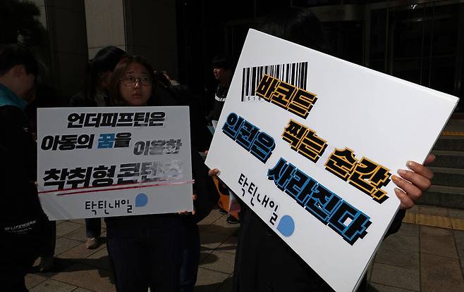 ‘탁틴내일’ 회원들이 ‘언더피프틴’ 방송 중단을 촉구하며 손팻말을 들고 있다. 프로그램 제작사는 “바코드는 학생증 콘셉트에서 가져온 것”이라고 해명했으나 “개인이 소지한 학생증의 바코드와 선정적으로 꾸며진 아동의 이미지에 바코드를 부착해 전시한 것은 본질에서 다르다”고 지적했다.