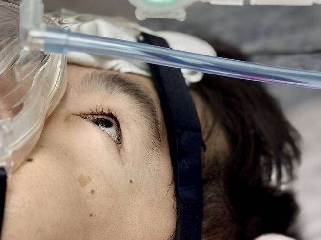 Jang Ik-seon lies in bed with his ventilator, his eyes sharp with focus — the same eyes that typed every word of his 70,000-character thesis through deliberate blinks. (Moon Joon-hyun/The Korea Herald)