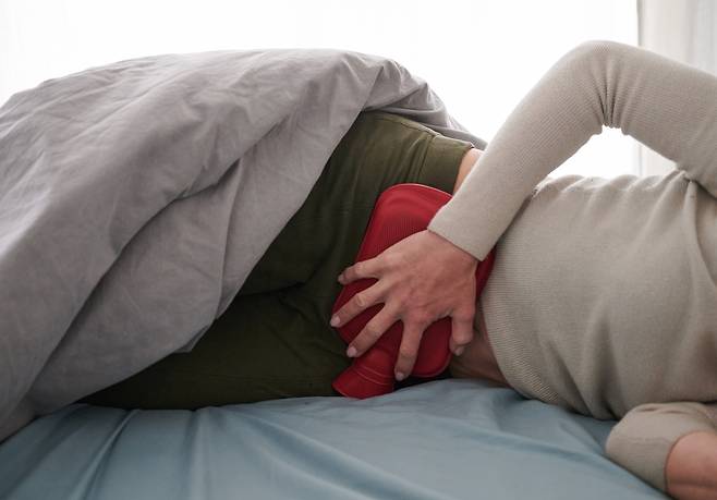 A person holds a hot water compress to her lower abdomen while lying in bed. (Getty Images)