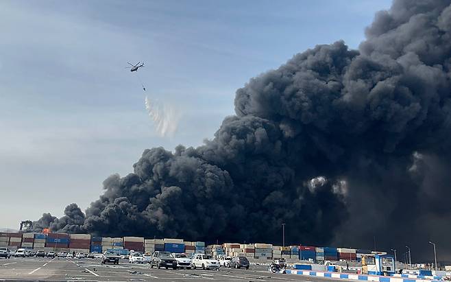26일 이란 남부 반다르아바스의 샤히드라자이 항구에서 대규모 폭발로 검은 구름이 일대를 뒤덮은 가운데 헬리콥터가 진화를 시도하고 있다. 반다르아바스=AP 뉴시스