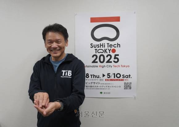 미야사카 마나부 도쿄도 부지사가 지난 12일 도쿄도가 주최하는 아시아 최대 규모의 스타트업 콘퍼런스 ‘스시테크 도쿄’ 포스터 앞에서 스시를 쥐는 포즈를 취하고 있다. 스시테크는 생선초밥이 아니라 ‘지속 가능한 첨단 도시 도쿄’(Sustainable High City Tokyo)의 약자로 도쿄 하면 누구나 떠올리는 음식인 ‘스시’를 연상시키는 중의적 표현으로 국제적인 인지도를 노렸다.