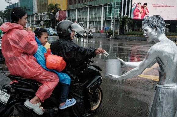 지난달 1일 인토네시아 자카르타의 한 도로에서 온몸을 은색 페인트로 칠한 아리 무난다르(오른쪽)가 비를 맞으며 오토바이 운전자에게 구걸하고 있다. AFP 연합뉴스