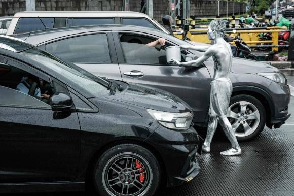 지난달 1일 인토네시아 자카르타의 한 도로에서 온몸을 은색 페인트로 칠한 아리 무난다르가 비를 맞으며 운전자에게 구걸하고 있다. AFP 연합뉴스