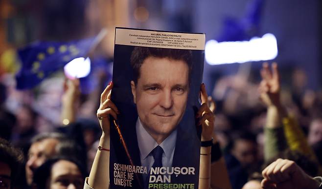 루마니아 대선 결선 1차 출구조사 결과가 발표된 19일 오전 수도 부쿠레슈티의 한 거리에서 시민이 이 도시의 시장인 니쿠쇼르 단 대통령 후보의 얼굴이 인쇄된 포스터를 흔들고 있다. /EPA 연합뉴스