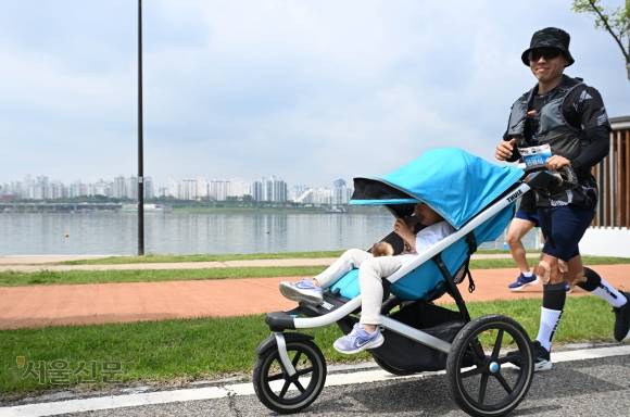 유모차를 끌고 ‘2025 서울신문 하프마라톤대회’에 참가한 아빠가 웃으며 달리고 있다. 홍윤기 기자