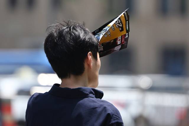 서울 한낮 기온이 26도까지 오른 14일 서울 종로구 광화문에서 한 시민이 전단지로 햇빛을 가리고 있다. 연합뉴스