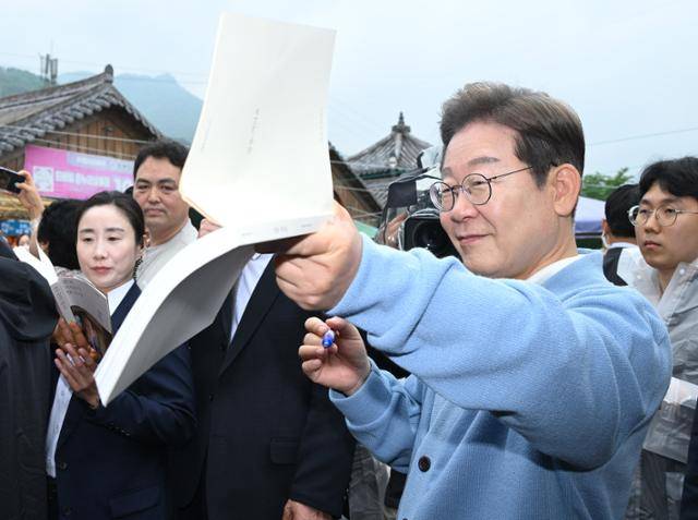 이재명 더불어민주당 대선 후보가 15일 경남 하동군 화개장터 노래비 앞에서 지지자가 내민 김혜경 여사의 저서 '밥을 지어요'에 서명하고 있다. 하동=고영권 기자