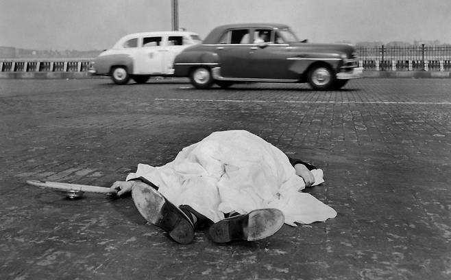 1939년 10월 29일 자동차 사고 희생자가 뉴욕 웨스트 사이드 고속도로 옆에 누워 천으로 덮여 있다. 자세히 보면 희생자는 천 밖으로 손과 발만 내놓고 오른손에는 운전대를 왼손은 천을 잡고 있다. 위지 촬영