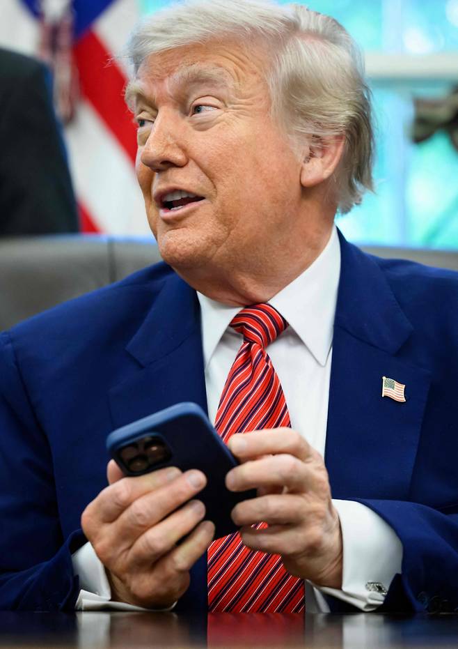 도널드 트럼프 미국 대통령이 23일(현지시간) 워싱턴 백악관에서 행정 명령에 서명을 하면서 취재진과 만나는 중 아이폰 벨 소리가 울리자 ‘무음 모드’로 바꾸고 있다. 2025.5.25 /AFPBBNews=뉴스1